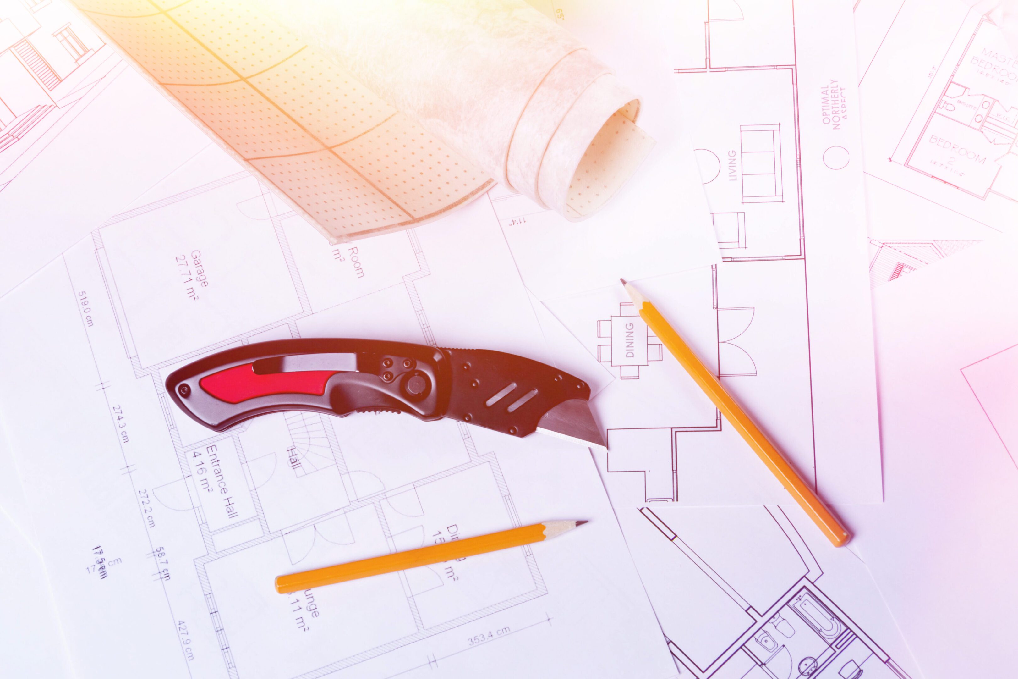 Blueprints with knife and pencils on table.