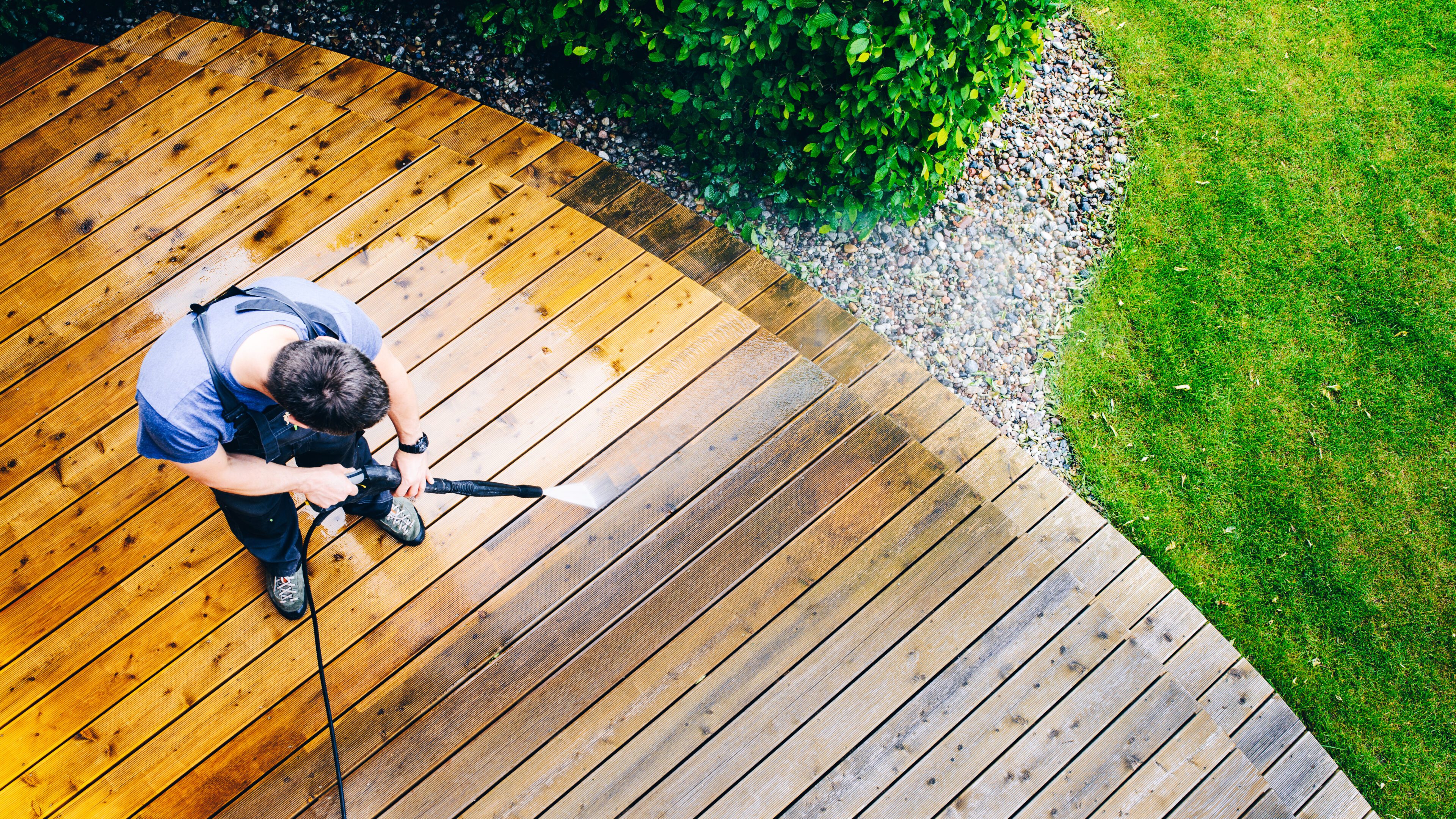 man cleaning terrace with a pressure washer man cleaning terrace with a power washer - high water pressure cleaner on wooden terrace surface