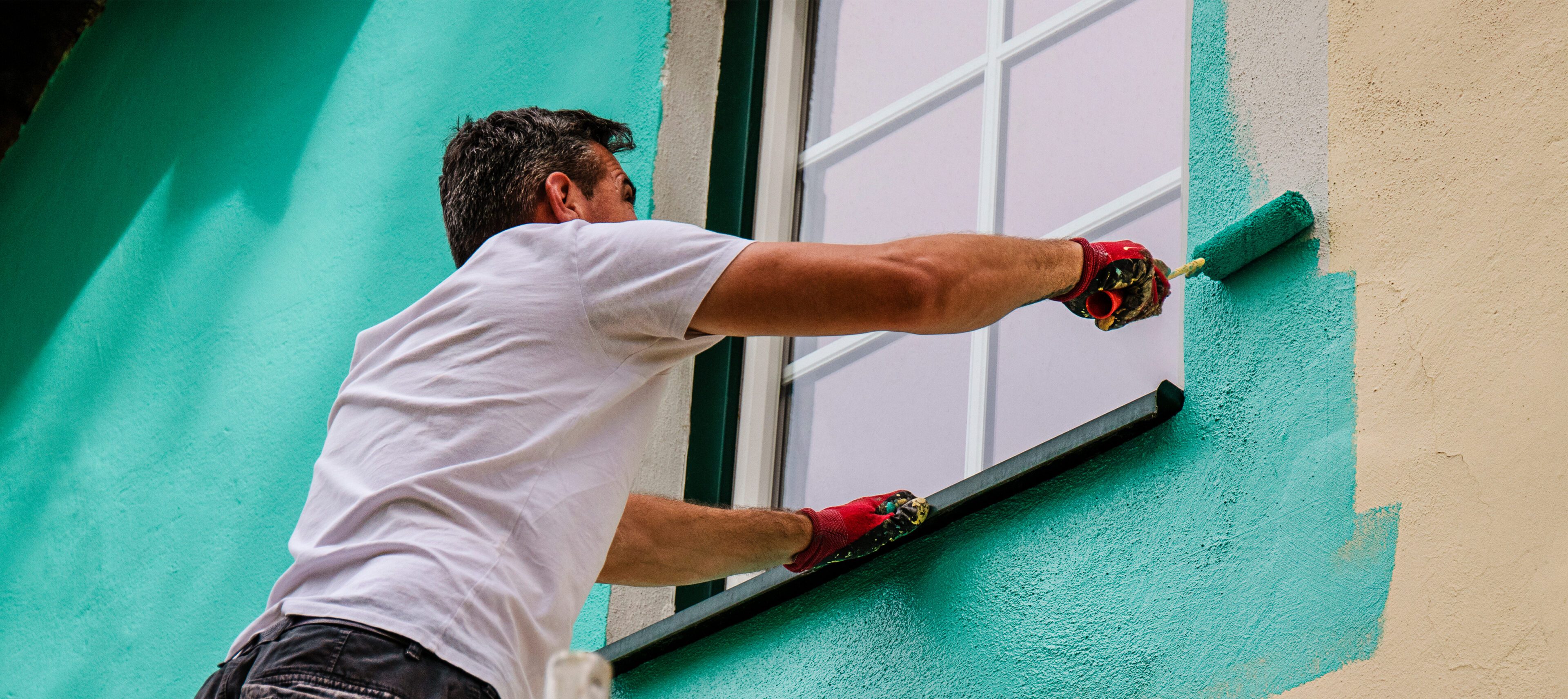 A worker paints the facade walls of a house with paint using a paint roller A worker paints the facade walls of a house with paint using a paint roller